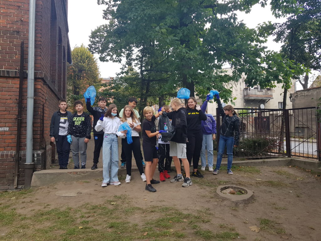 Uczniowie stoją przed szkołą z workami na śmieci